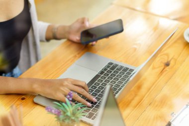 Akıllı telefondan müşterilere mesaj göndermekle, bilgisayarla online bilgileri kontrol etmekle meşgul bir kadın.