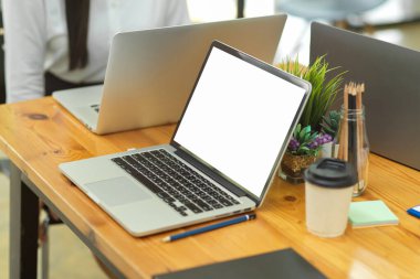 Boş ekran, 2 dizüstü bilgisayar, kahve fincanı, kırtasiye malzemesi ve ahşap masa dekorasyonu.