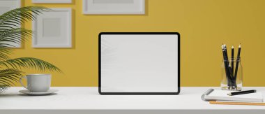 Şık, yaratıcı çalışma alanı sarı duvarda, beyaz masa ve ev bitkilerinde kırtasiye malzemesi olan boş tablet ekranda, duvarda boş çerçeve, 3D görüntüleme, 3D resimleme