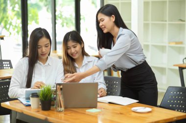 Genç iş gurubu, bilgisayarla tabletteki mali verileri tartışıyor ve özetliyor ve ofis odasındaki ahşap masada raporlar sunuyor.