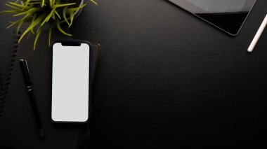 Akıllı telefon boş ekran modeliyle siyah arkaplan ve kalem, siyah defter, ev bitkisi, tablet, modern çalışma alanını kapat