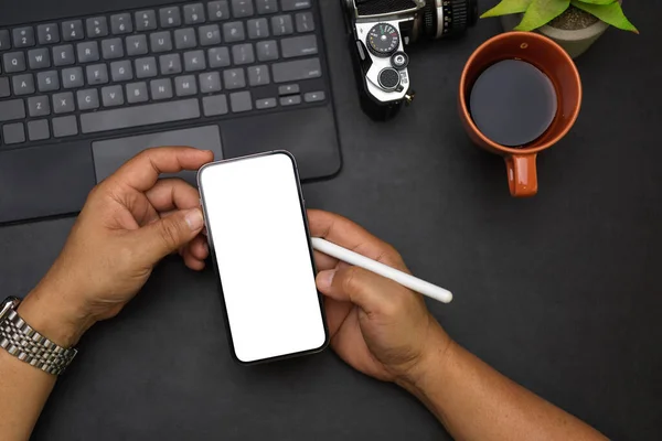 Close up, overhead male hands, reading news on the internet via smartphone, smartphone white screen mockup, coffee in the morning, tablet, camera, black workspace
