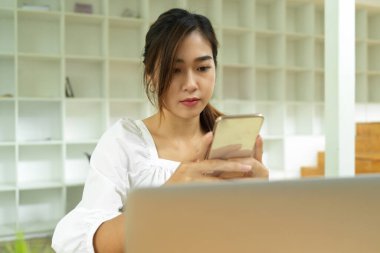 Genç Asyalı kadın akıllı telefondan mesaj gönderiyor, iş bilgilerine göz atıyor, sohbet ediyor.