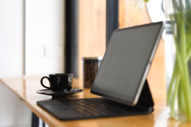 Yan görüş, klavyeli dijital tablet siyah ekran, kahve fincanı, cam pencerenin yanındaki kafede taşınabilir.