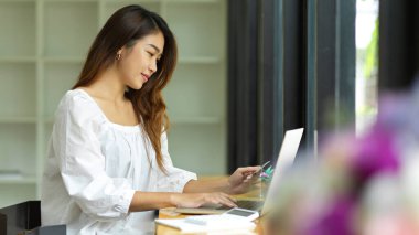 Kredi kartı tutan, dizüstü bilgisayar kullanan, para harcayan, e-ticaret yapan, online bankacılık yapan, online alım yapan bir kız. 