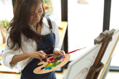 Genç bir kız öğrenci akrilik boyayla resim yapıyor, resim malzemeleri, palet tutuyor, yaratıcı bir hobi.