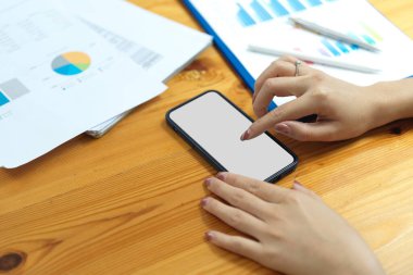 Kapanış, akıllı telefon kullanan iş kadını, telefon ekranına dokunan, internetteki bilgileri karıştıran, iş müşterisine mesaj bırakan, masadaki iş evrakları.