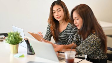 İş adamlarından biri kağıt panoya not alırken meslektaşı ofisteki dizüstü bilgisayardan fikri araştırıyor.