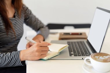 Yan görünüş, iş kadını dizüstü bilgisayara bakarken not alıyor, laptop boş ekran modeli, kahve dükkanında çalışıyor.
