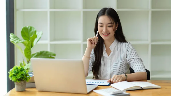 年轻的女商人拿着笔 看着手提电脑屏幕 阅读电子邮件 思考如何获得创意 在现代化的办公室工作 — 图库照片