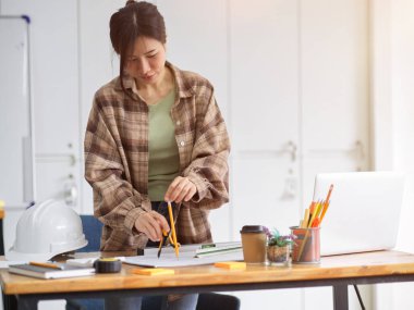 Ofiste çalışan Asyalı kadın inşaat mühendisi, planlı pusula kullanıyor. 