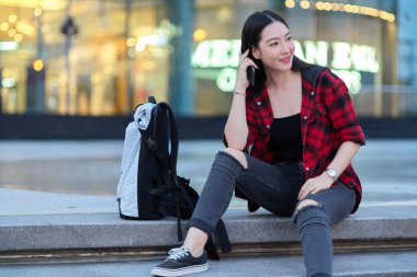 Şehir alışveriş merkezinin merdivenlerinde gece vakti sırt çantasıyla oturan şık, genç bir turist kadın, birinin gelip seni almasını bekliyor. 