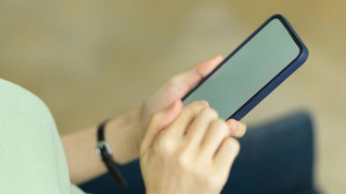 Beyaz ekran maketi ve bulanık arkaplanı olan akıllı telefonu tutan, daktilo eden ve sohbet eden bir kadın.