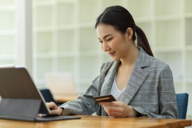 Asyalı genç girişimci para transferi için dijital tablet kullanıyor. Kredi kartı tutuyor. İnternet bankacılığı, internet hizmeti