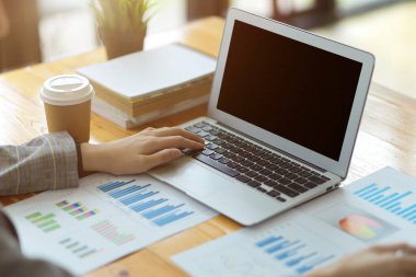 Konsantre olmuş genç ve güzel iş kadınının parlak modern ofiste dizüstü bilgisayar ve finansal veri kağıtları üzerinde çalışmasının ekili fotoğrafı.