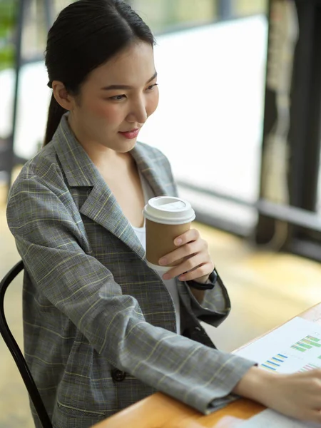 Focused young businesswoman sit and work on desk while drinking coffee in office, asian business female worker working on laptop