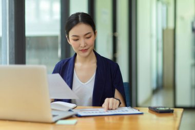 Zarif iş kadını veri analizi ve proje yönetimi için dizüstü bilgisayar kullanıyor, modern ofis odasında çalışıyor, iş veri tablosu üzerinde çalışıyor