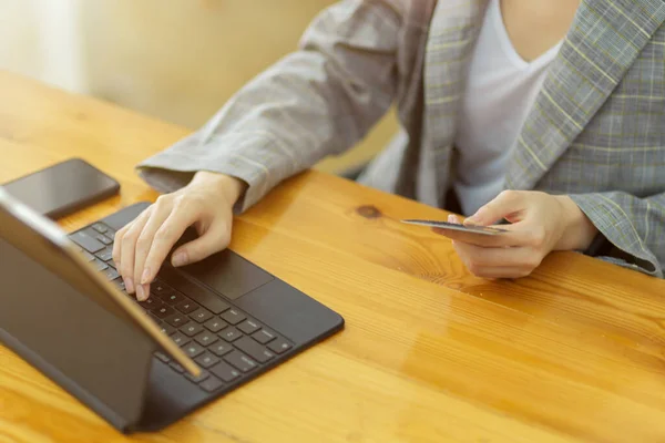 Crop image of female freelancer holding credit card and typing on tablet keyboard for buying online goods, transfer money