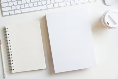 Beyaz boş kitap kapağı ve beyaz arka planda klavye bilgisayarı ve beyaz kahve fincanı. Üst görünüm