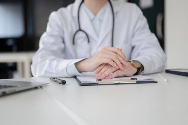 Steteskoplu bir doktor, panoyu belgelerle dolduruyor, teşhis odasında, hastanede ya da klinikte beyaz masada oturuyor..