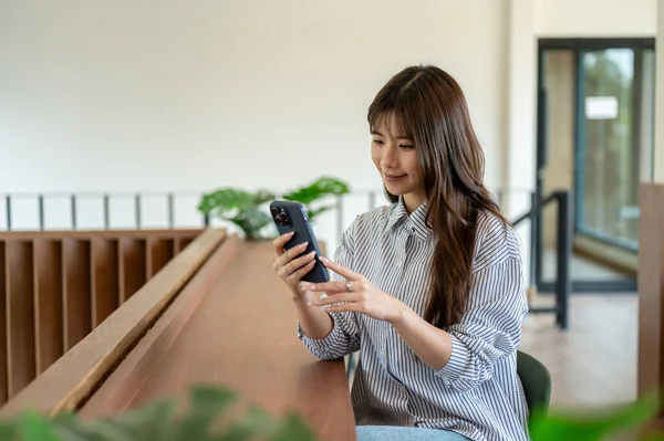 Kafede ya da kütüphanede ahşap tezgahta otururken akıllı telefonuna bakıp gülümseyen Asyalı kadın. Dinleniyorum, dışarıda dinleniyorum..