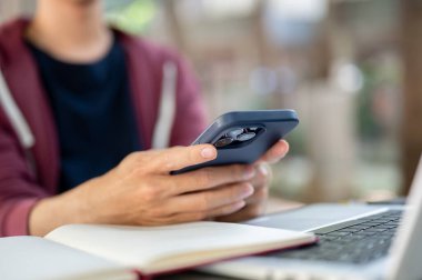 Beton masada otururken akıllı telefonu açık bir defter ve dizüstü bilgisayarın üzerinde tutan eli kapat. Bakıyor ya da yazıyor, Çalışıyor ya da Çalışıyor.