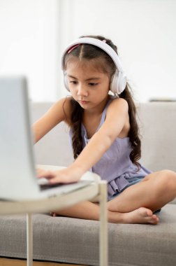 Mor gömlekli Asyalı bir çocuk ya da kız, beyaz masada otururken dizüstü bilgisayarında yazı yazıyor. Video izlemek ya da müzik dinlemek.