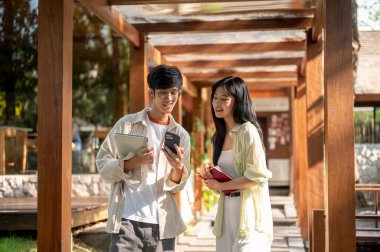 Gülen Asyalı kadın ve erkek arkadaşı ahşap koridorda gülen yüzlü telefona bakıyor. Çalışmak ya da dışarıda okumak, Garden Cafe ya da Restoran.