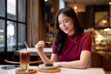 Genç Asyalı kadın kaşık tutarak kafede portakallı kahve fincanı yiyor. Yiyecek ve içecek, estetik kafe, tavsiye..