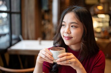 İki elinle tiramisu bardağı tutan güzel Asyalı bir kadın kafede otururken gözlerini kaçırıyor. Tatlı Tatlı Tatlı, Estetik Kafe, Dükkan Tavsiyesi.