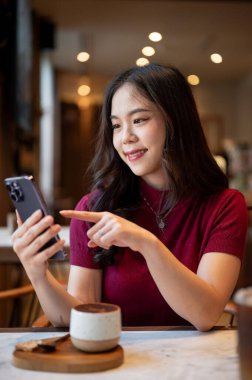 Bir kafede otururken Tiramisu bardağının üzerinden akıllı telefona bakıp işaret eden Asyalı kadını kapatın. Tatlı Tatlı Tatlı, Estetik Kafe, Dükkan Tavsiyesi.