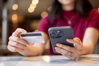 Bulanık bir kadının kafedeki mermer masada elinde akıllı telefonuyla kredi kartına bakması. Promosyon, Banka Reklamcılığı, Nakitsiz Toplum.