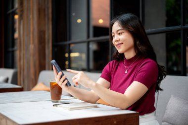 Asyalı bir kadın bakar ve telefonu işaret eder kahve hariç kafedeki kanepede oturur. Dışarısı soğuk, Estetik Kafe, Şehir Hayatı.