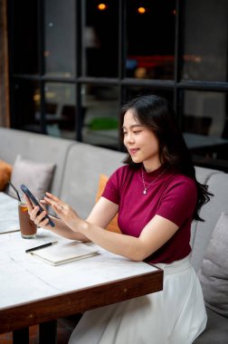 Gülümseyen Asyalı kadın kahveyi bir kenara bırakırsak kafedeki koltukta oturuyor gibi görünüyor. Dışarısı soğuk, Estetik Kafe, Şehir Hayatı.