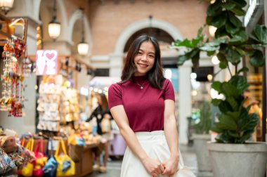 Kapalı bir markette ya da alışveriş merkezinde hediyelik eşya arabasının yanında duran Asyalı kadın turist. Ödeme günü tanıtımı, seyahat gezisi, turistik yerler..