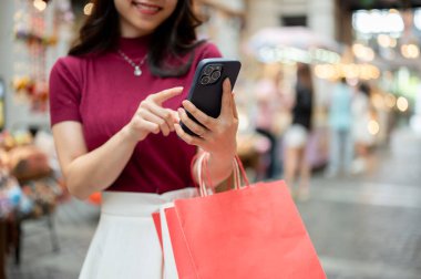 Alışveriş torbası tutan kadın müşterinin markette ya da alışveriş merkezinde beklerken telefona baktığı yakın çekim. Ödeme günü tanıtımı, seyahat gezisi, turistik yerler..