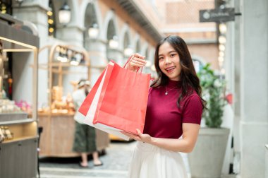 Kapalı bir markette ya da alışveriş merkezinde durup alışveriş torbalarını gösteren gülümseyen Asyalı kadın. Ödeme günü tanıtımı, seyahat gezisi, turistik yerler..