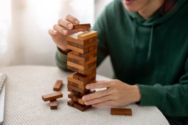 Yuvarlak masada tek başına oynayan bir adamın elini, tahta bloklu oyuncak kulesinin tepesine koy. Parti oyunu, geliştirme oyuncakları, öğrenme etkinliği.