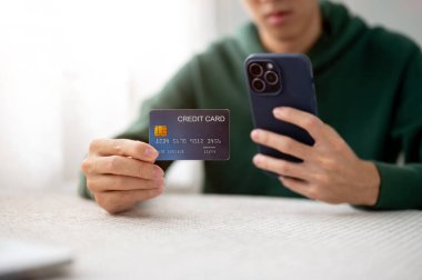 Bir adamın elinde tuttuğu ya da kredi kartını gösterip kafede otururken telefona baktığı bir fotoğraf. Nakitsiz Toplum, Banka Reklamcılığı, Şehir Hayatı.