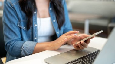 Kafedeki masada otururken bir kadının ellerini dizüstü bilgisayarla tutup akıllı telefonu kullanırken. Çevrimiçi Freelancer, Modern Teknoloji, Şehir Hayatı.