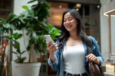 Asyalı bir kadın yürürken ya da alışveriş merkezinde ya da markette dururken telefon askısı tutuyor. Yalnız Seyahat, Turist Çekimleri, Unutulmaz Yolculuk.
