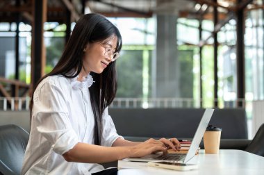 Dizüstü bilgisayarında yazan gözlüklü Asyalı bir kız öğrenci. Kitaplar bir yana, kafede kahve masasında oturuyor. Serbest Çalışan veya Çalışan, Modern Şehir Hayatı.