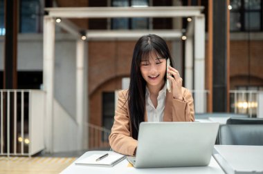 Asyalı iş kadını ya da ofis çalışanı kafedeki masada dizüstü bilgisayarla konuşuyor. Profesyonel Takım Elbise, Uzaktan Çalışma, Günlük Yaşam.