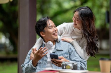 Genç Asyalı bir çift birbirlerine gülümserken açık masada otururken erkeğin omzuna sarılıyorlar. Randevu aktivitesi, Şehir Hayatı, Serinlemek Açık Hava