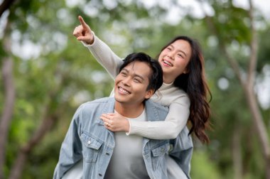 Genç Asyalı bir çift, parkta yürürken erkeğin omzunu işaret ediyor. Randevu aktivitesi, doğa iyileştirme, dışarıda dinlenme..