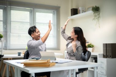 Asyalı işadamı ve kadın iş arkadaşı ofisteki bir tabletin önünde beşlik çakıyor. Şirket işleri, Modern Şirket, Proje Ekibi.