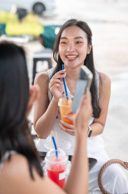 Güzel Asyalı kadın elinde meyve suyu bardağıyla markette bir arkadaşıyla otururken konuşuyor. Seyahat, Turizm, Tatil Tatili.