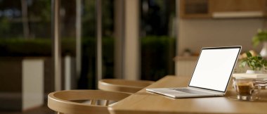 Boş ekran dizüstü bilgisayar ve cam duvarlı bir kafede koltuklu ahşap masada bir bardak kahve. Reklam modeli, 3D çizim, 3D illüstrasyon.