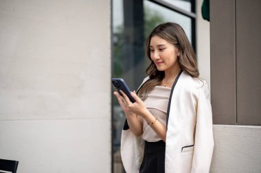 Uzun saçlı Asyalı kadın binanın direğinde dikilirken akıllı telefonundan gülümsüyor. Yayını kontrol ediyorum, Şehir Hayatı, Dışarıdaki Serinleme.