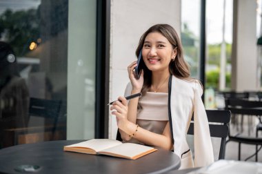 Kafede ya da kahve dükkanında siyah bir masada açık bir kitapla otururken telefonda konuşurken gülümseyen Asyalı kadın. Çalışıyorum ya da çalışıyorum, dışarıda takılıyorum..